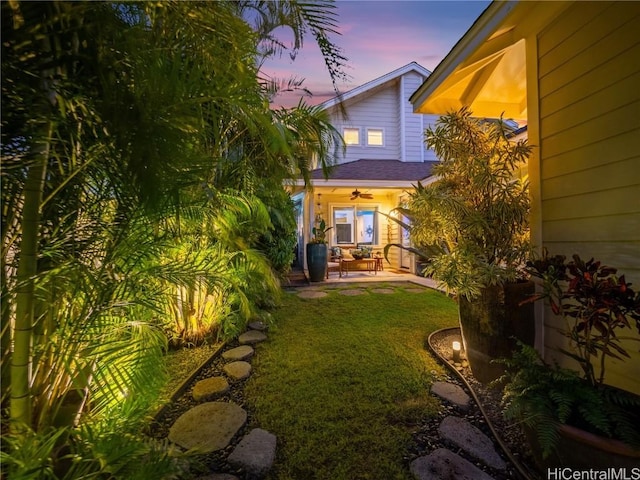 yard at dusk featuring ceiling fan and a patio area