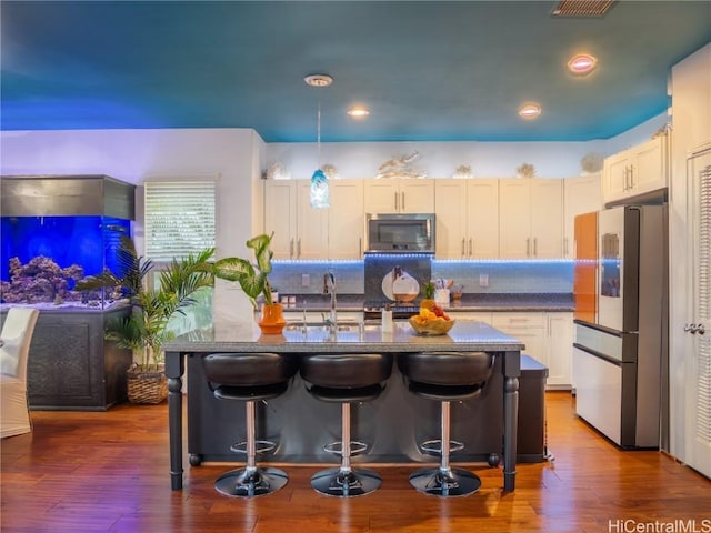 kitchen featuring decorative light fixtures, dark wood-type flooring, fridge, and a center island with sink