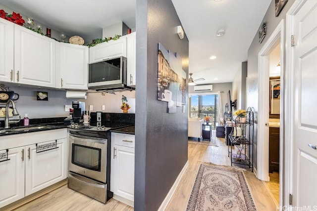 kitchen with a wall mounted air conditioner, sink, white cabinetry, and stainless steel appliances