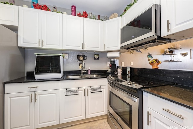 kitchen featuring white cabinets, stainless steel appliances, dark stone counters, and sink