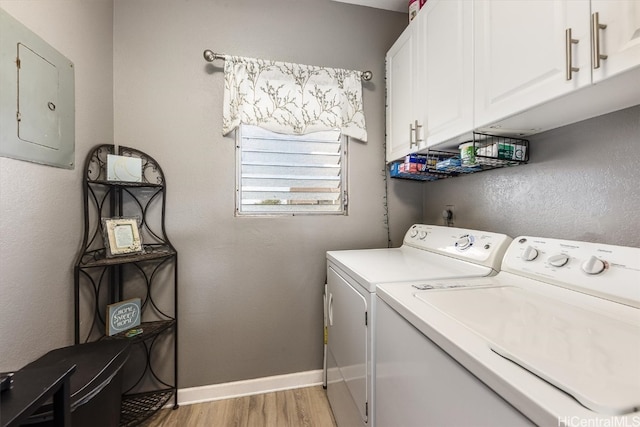 clothes washing area featuring electric panel, washer and dryer, light hardwood / wood-style flooring, and cabinets