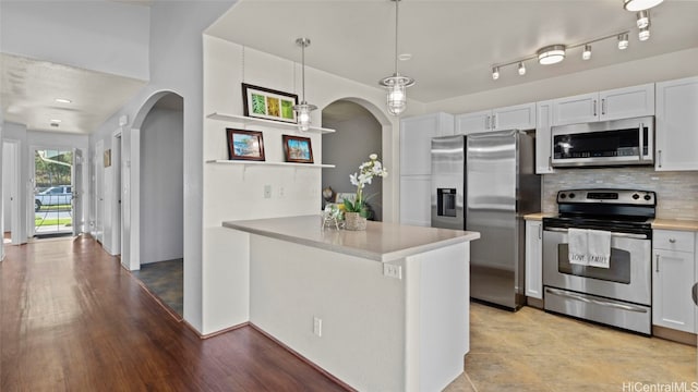 kitchen with kitchen peninsula, white cabinets, decorative light fixtures, light wood-type flooring, and appliances with stainless steel finishes