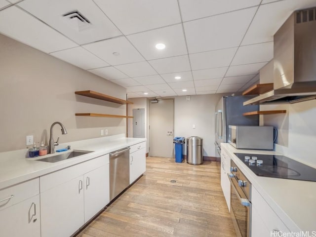 kitchen featuring sink, light hardwood / wood-style flooring, wall chimney exhaust hood, appliances with stainless steel finishes, and white cabinetry