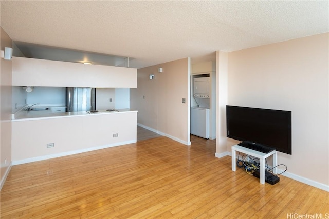 living room with a textured ceiling, stacked washer / drying machine, sink, and light hardwood / wood-style flooring