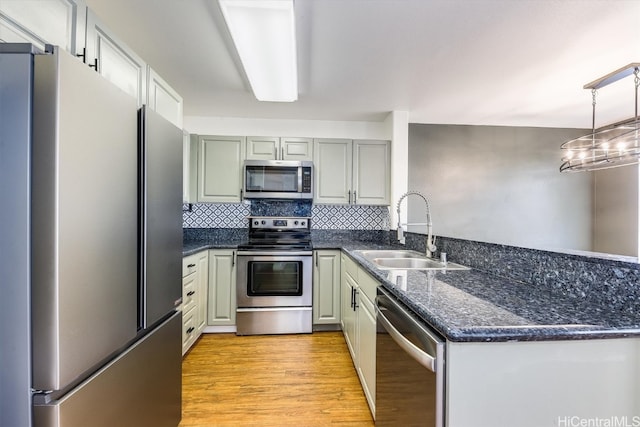 kitchen with decorative backsplash, appliances with stainless steel finishes, sink, light hardwood / wood-style floors, and decorative light fixtures