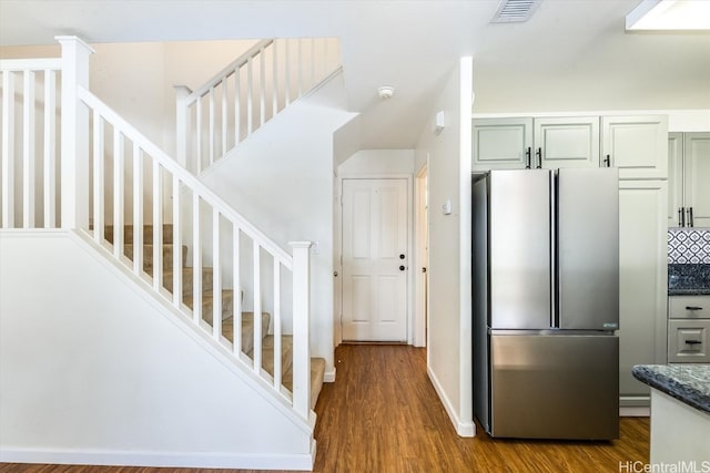 kitchen featuring dark stone countertops, stainless steel fridge, hardwood / wood-style flooring, and tasteful backsplash