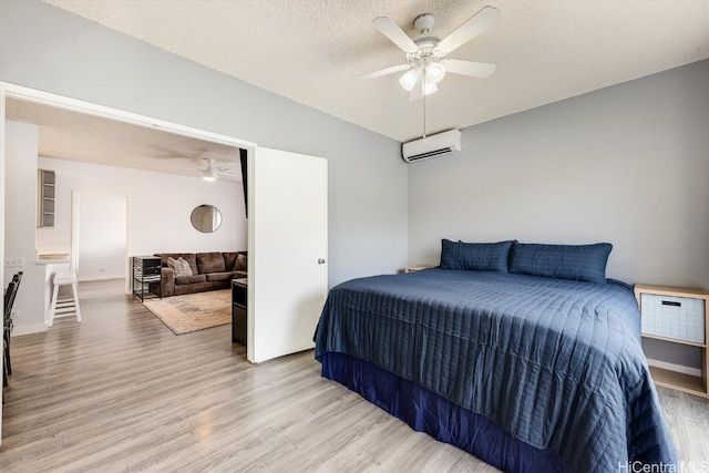 bedroom with a textured ceiling, light hardwood / wood-style flooring, a wall mounted AC, and ceiling fan