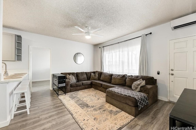 living room with a wall mounted air conditioner, sink, hardwood / wood-style flooring, ceiling fan, and a textured ceiling