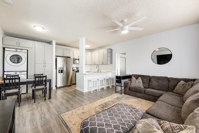 living room with a textured ceiling, stacked washing maching and dryer, light hardwood / wood-style flooring, and sink