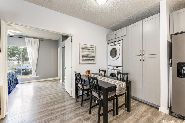 dining room featuring ceiling fan, light hardwood / wood-style flooring, stacked washing maching and dryer, and a textured ceiling