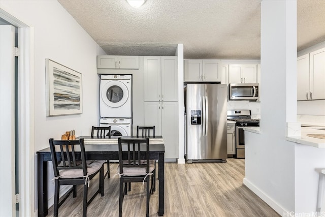 dining space featuring a textured ceiling, light hardwood / wood-style flooring, and stacked washer / drying machine