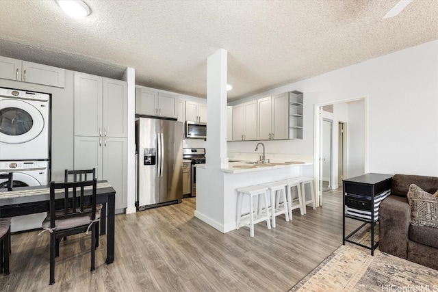 kitchen with a breakfast bar, stacked washer and clothes dryer, a textured ceiling, appliances with stainless steel finishes, and kitchen peninsula