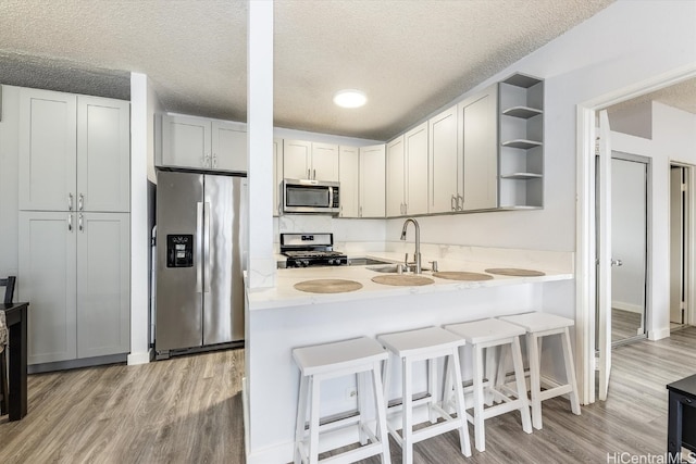 kitchen featuring sink, a textured ceiling, light hardwood / wood-style floors, kitchen peninsula, and stainless steel appliances