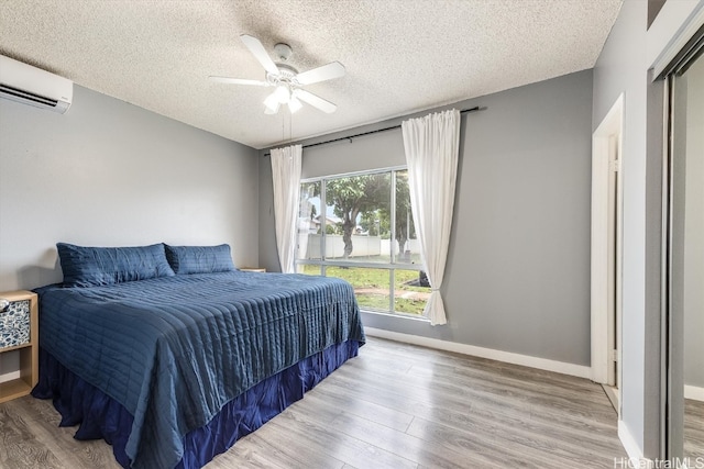 bedroom featuring light wood-type flooring, a textured ceiling, a wall unit AC, and ceiling fan