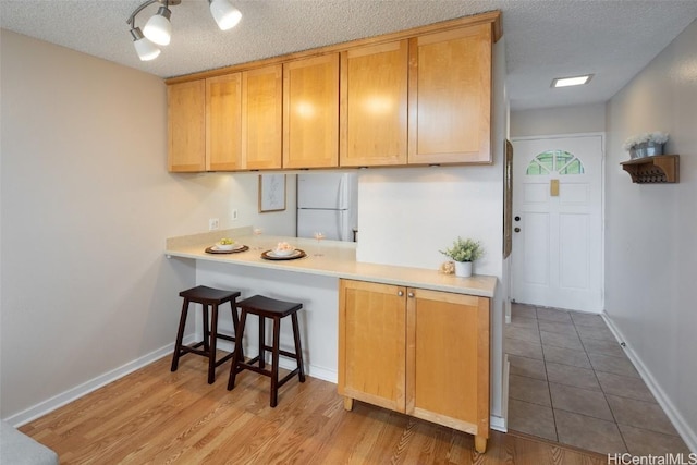 kitchen with kitchen peninsula, white fridge, light wood-type flooring, and a textured ceiling