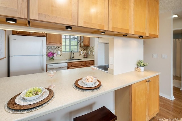 kitchen featuring sink, tasteful backsplash, light hardwood / wood-style floors, white appliances, and light brown cabinetry