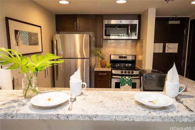 kitchen featuring appliances with stainless steel finishes, dark brown cabinetry, tasteful backsplash, and light stone countertops