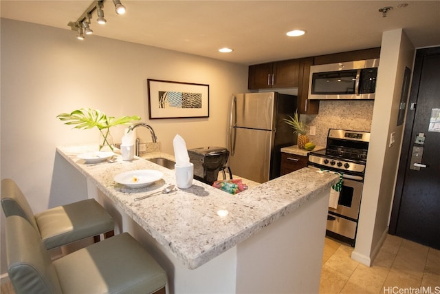 kitchen featuring sink, a kitchen bar, kitchen peninsula, stainless steel appliances, and decorative backsplash