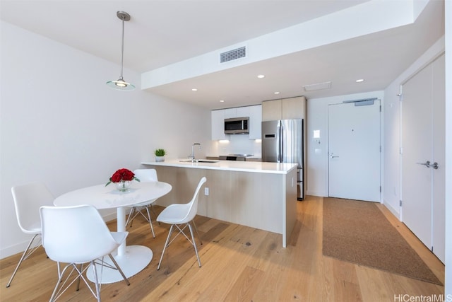 kitchen with appliances with stainless steel finishes, light wood-type flooring, sink, pendant lighting, and white cabinetry