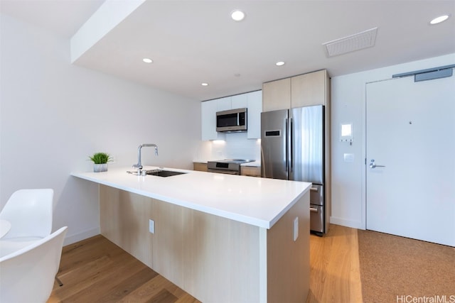 kitchen with kitchen peninsula, light hardwood / wood-style flooring, stainless steel appliances, and sink