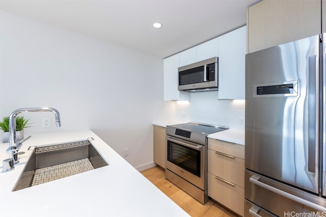 kitchen featuring white cabinetry, sink, tasteful backsplash, light hardwood / wood-style floors, and appliances with stainless steel finishes