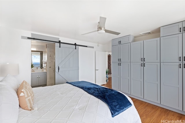 bedroom featuring ceiling fan, a barn door, ensuite bathroom, light wood-type flooring, and a closet