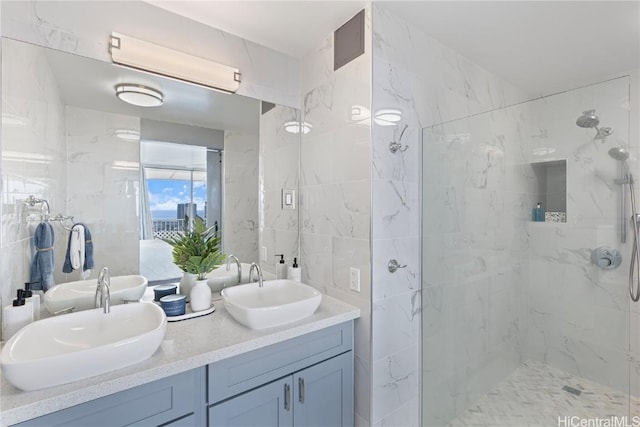 full bathroom featuring double vanity, a marble finish shower, tile walls, and a sink