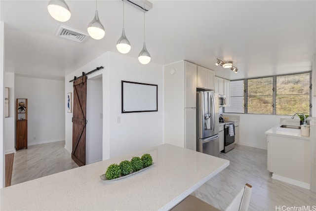 kitchen featuring pendant lighting, white cabinetry, stainless steel appliances, sink, and a barn door