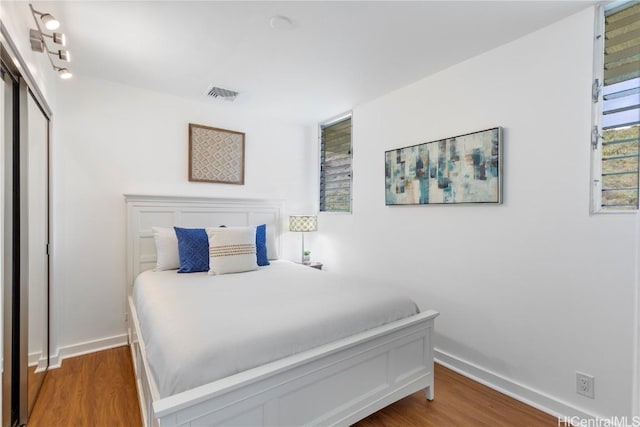 bedroom with a closet, visible vents, baseboards, and wood finished floors