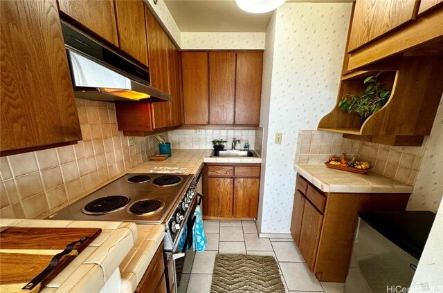 kitchen with sink, tasteful backsplash, tile countertops, light tile patterned floors, and electric range