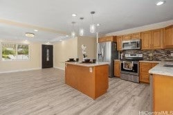 kitchen with decorative backsplash, hanging light fixtures, light wood-type flooring, stainless steel appliances, and a center island