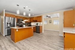 kitchen with appliances with stainless steel finishes, a kitchen island, pendant lighting, ornamental molding, and light hardwood / wood-style flooring