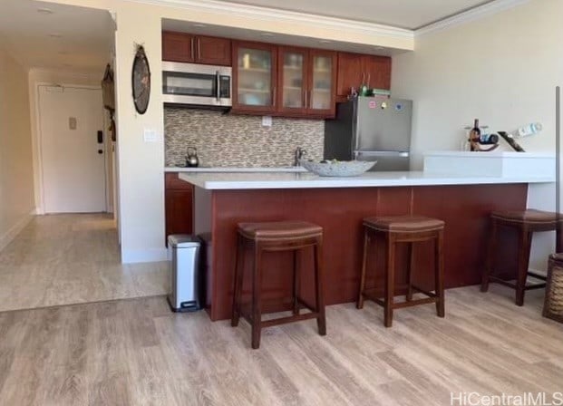 kitchen featuring kitchen peninsula, backsplash, light wood-type flooring, crown molding, and stainless steel appliances