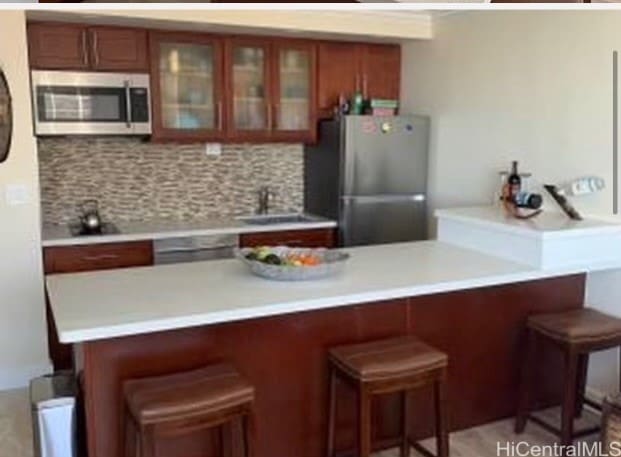 kitchen featuring tasteful backsplash, sink, a kitchen bar, kitchen peninsula, and stainless steel appliances