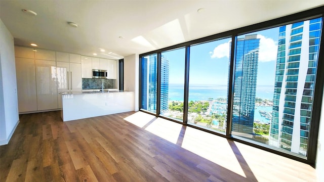 kitchen with decorative backsplash, wood finished floors, floor to ceiling windows, stainless steel microwave, and white cabinetry