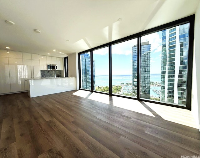 unfurnished living room featuring dark wood-style flooring, a sink, recessed lighting, a water view, and floor to ceiling windows