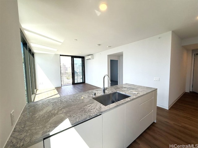 kitchen featuring white cabinets, light stone counters, dark hardwood / wood-style floors, a wall of windows, and sink