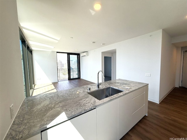 kitchen featuring light stone countertops, dark wood finished floors, a wall mounted air conditioner, a sink, and white cabinets