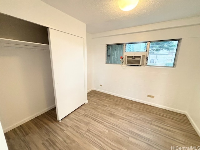 unfurnished bedroom with a closet, cooling unit, a textured ceiling, and hardwood / wood-style floors