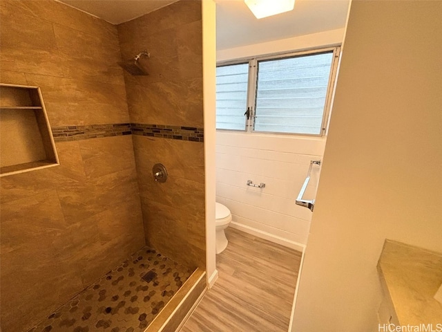 bathroom with toilet, wood-type flooring, and tiled shower