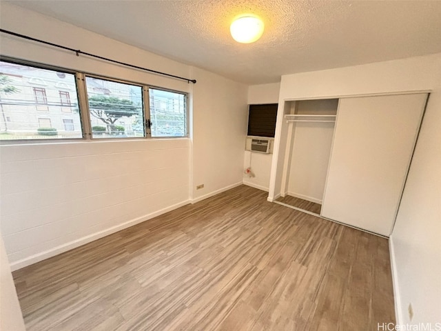 unfurnished bedroom with a textured ceiling, cooling unit, hardwood / wood-style flooring, and a closet