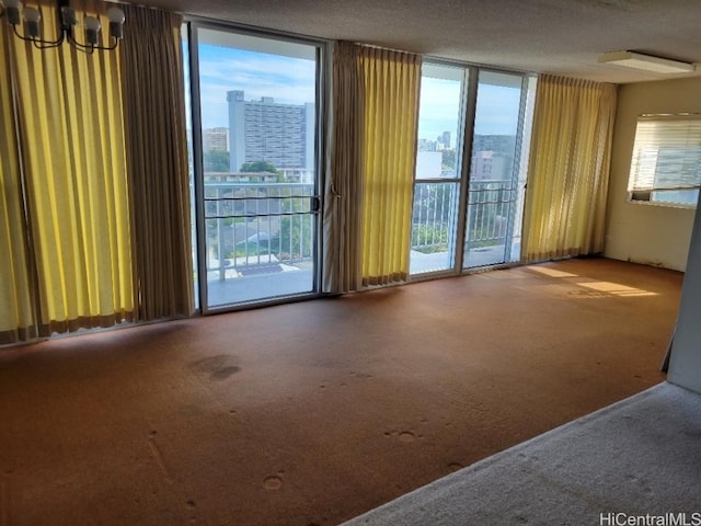 carpeted spare room with a notable chandelier, a textured ceiling, and a wealth of natural light