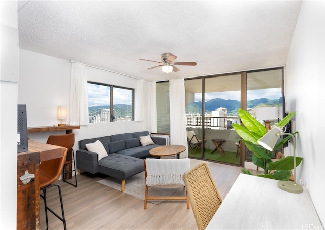 living room featuring a mountain view, a textured ceiling, light wood-type flooring, and ceiling fan