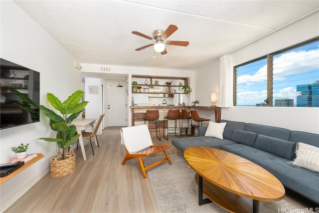 living room featuring light hardwood / wood-style flooring, a textured ceiling, and ceiling fan