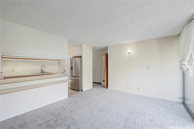 unfurnished living room with light carpet, a textured ceiling, and sink