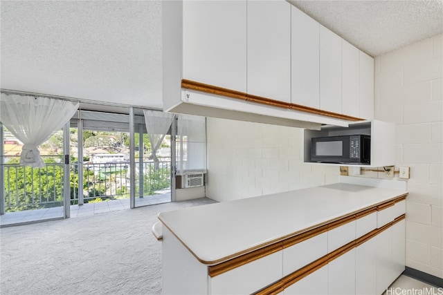 kitchen featuring a textured ceiling, kitchen peninsula, light colored carpet, and white cabinets