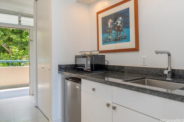 kitchen with white cabinets, sink, dark stone counters, and stainless steel refrigerator