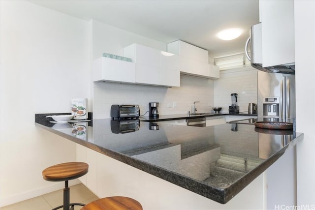 kitchen with kitchen peninsula, white cabinets, backsplash, a breakfast bar area, and dark stone counters