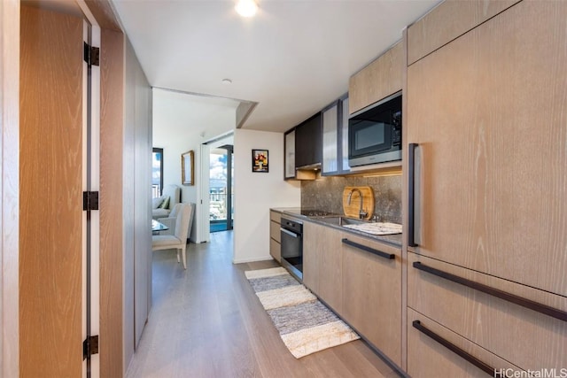 kitchen with tasteful backsplash, a sink, light wood-type flooring, built in microwave, and oven