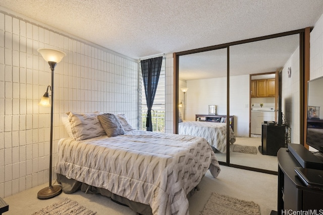 bedroom featuring washer / dryer, a textured ceiling, a closet, light carpet, and tile walls